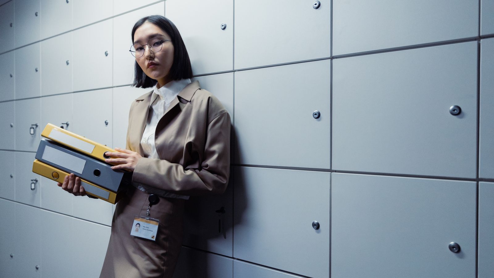 Businesswoman in office attire standing with documents, appearing poised in a modern office setting.