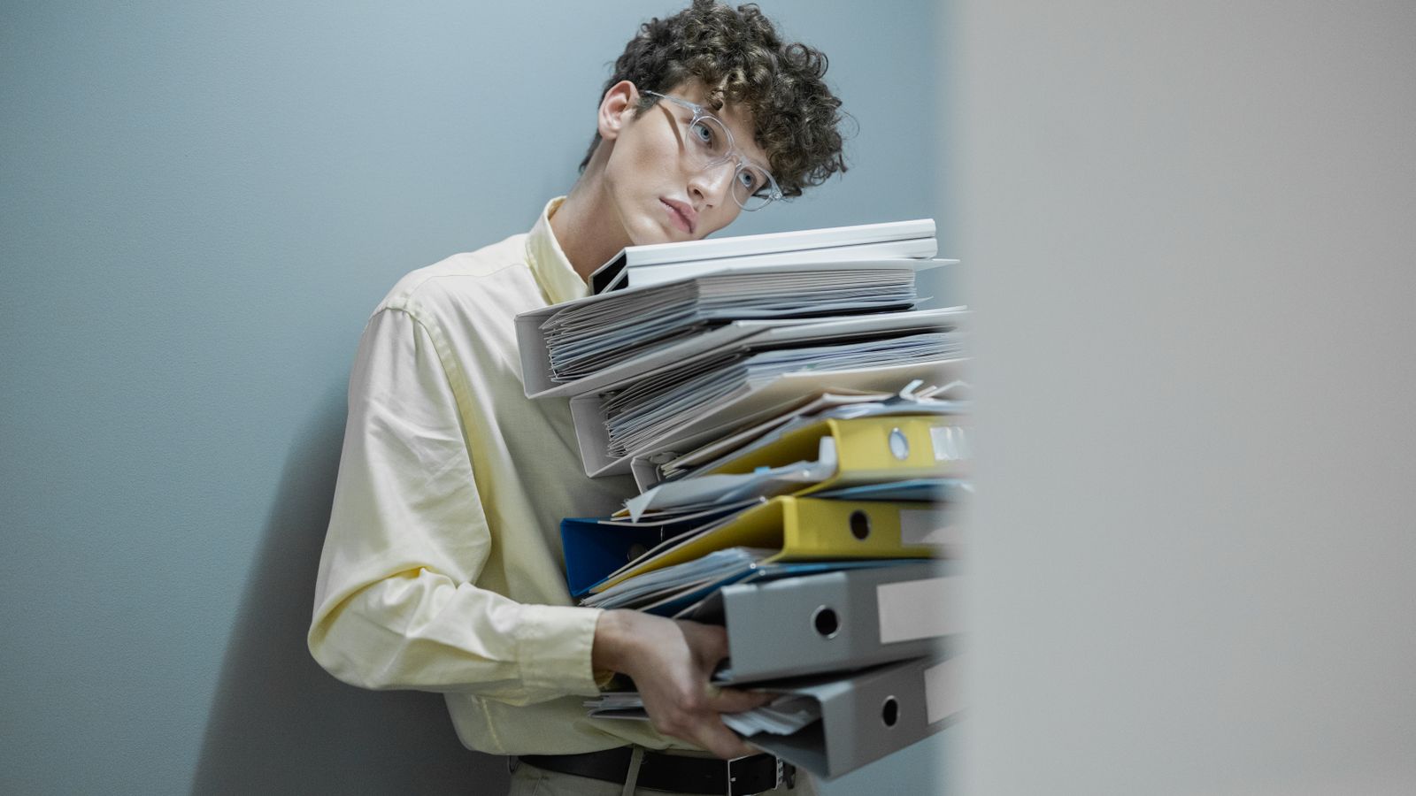 Young man overwhelmed with a stack of folders symbolizes workplace stress.